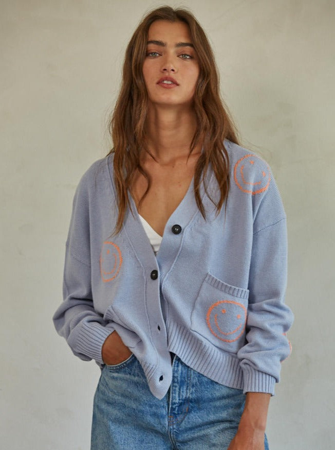 Snapshot Smiley Cardigan Knit Sweater Cotton Acrylic Smile Motif Detailed Button Down Long Sleeve Cardigan Top With Front Pockets 60% Cotton, 40% Acrylic Color: Light Blue The Snapshot Smiley Cardigan offers a lightweight option for extra warmth, thanks to its cozy knit fabric. This cardigan features a unique smiley face design, complete with a button-up closure. An eye-catching piece, this cardigan is perfect for those looking to add a playful touch to their wardrobe.